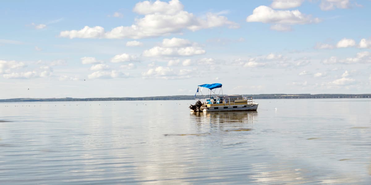 A small boat with a blue canopy floats on a calm lake under a partly cloudy sky.