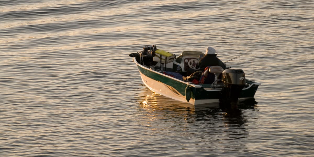 A fisherman in a small boat navigates calm waters during sunrise.