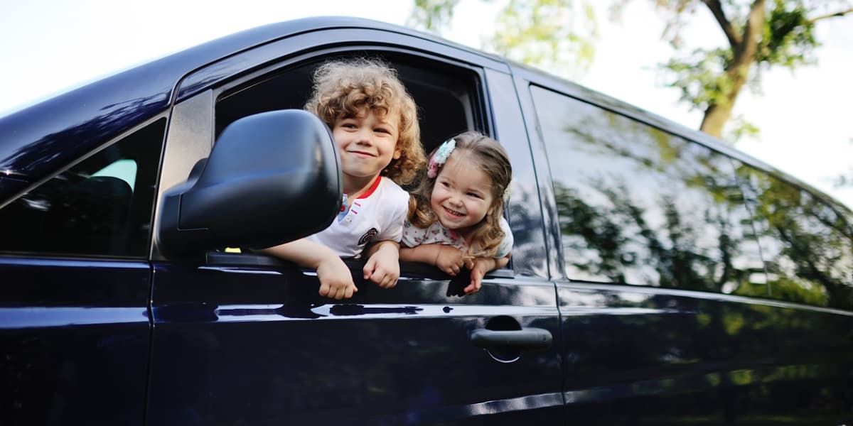 Two happy children are peeking out of the window of a blue van.