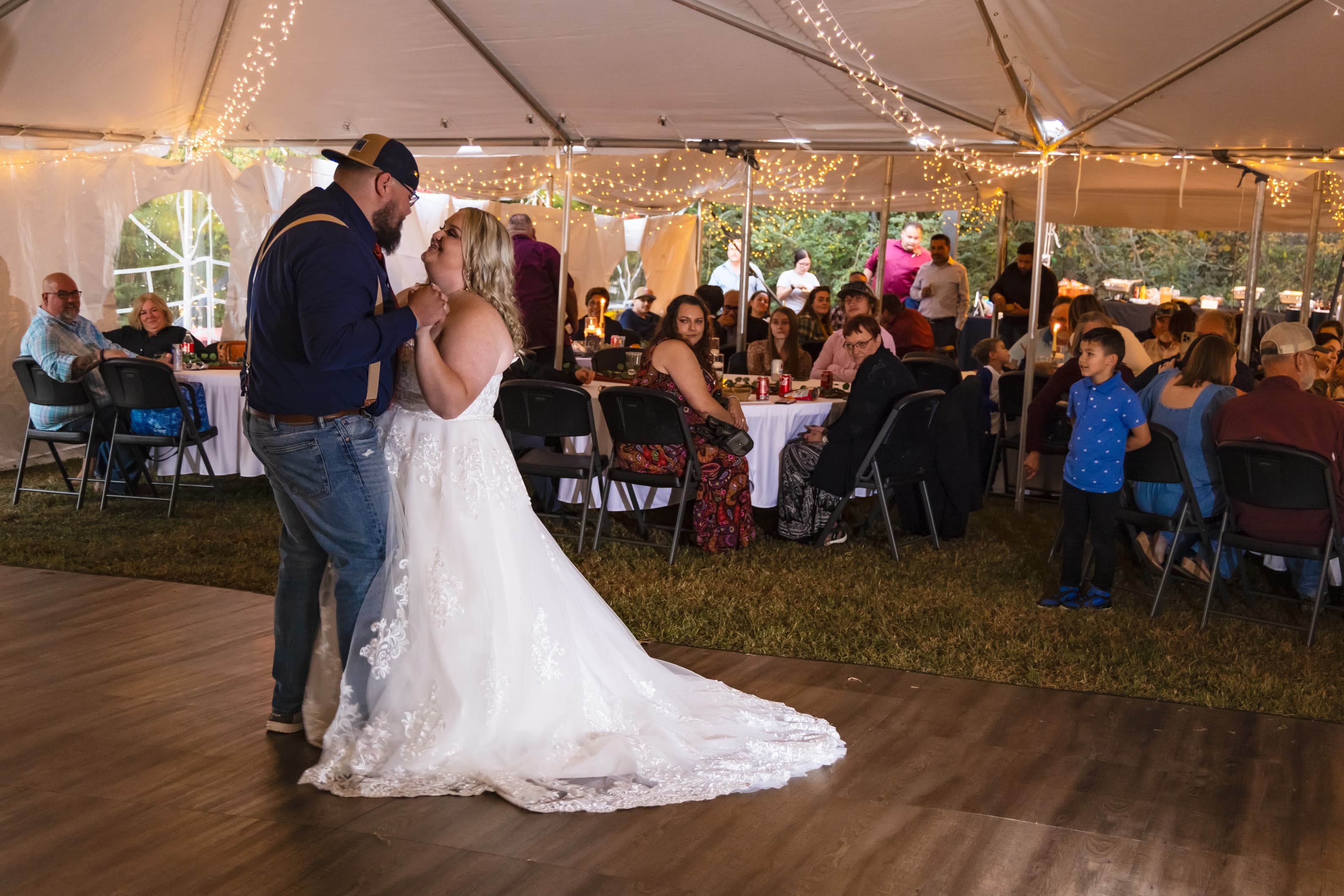 A bride and groom dance together under a tent filled with guests, celebrating their wedding.