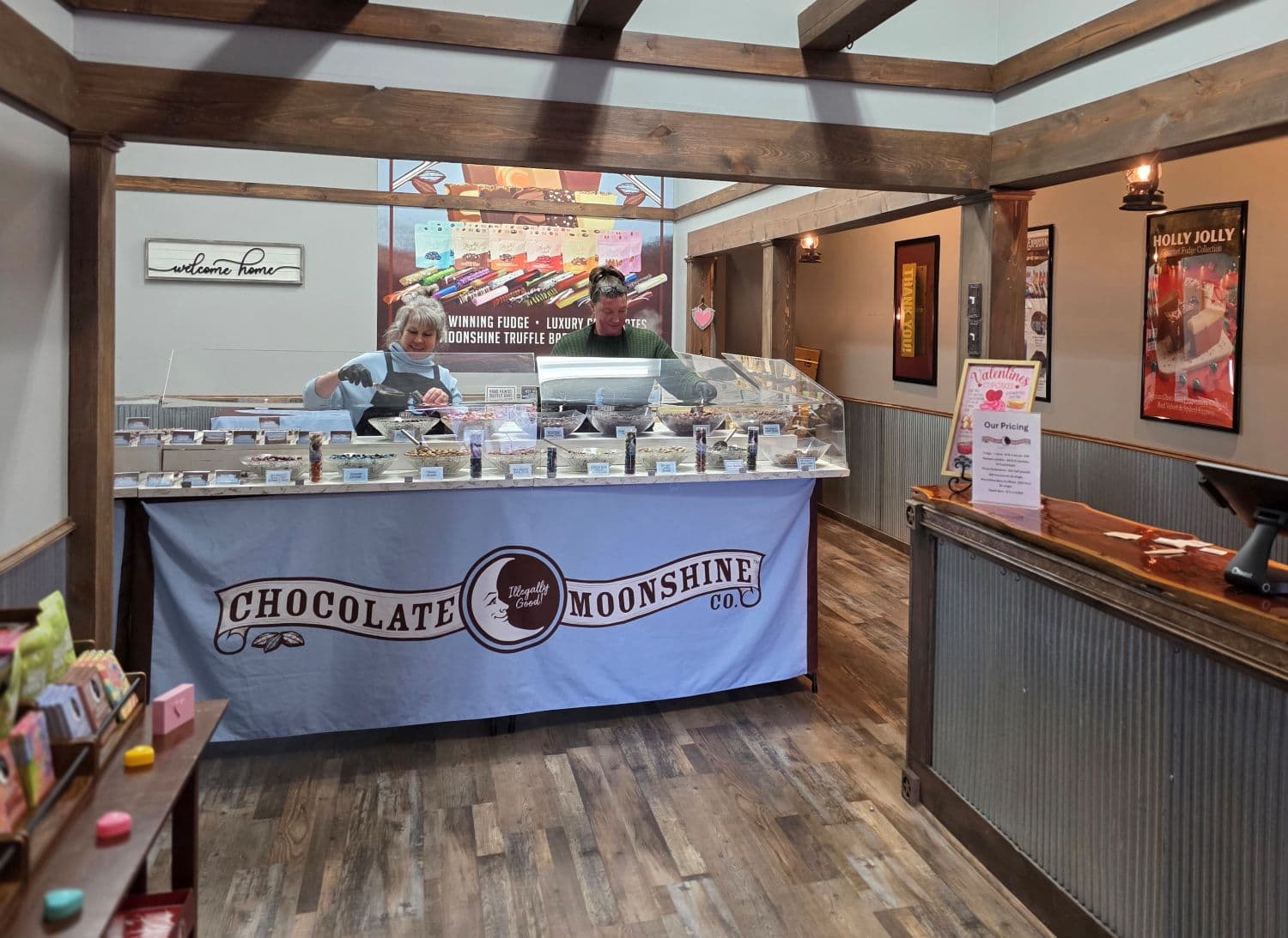 Interior of a chocolate shop featuring a display of confections and two employees behind the counter. Interior of a chocolate shop featuring a display of confections and two employees behind the counter.