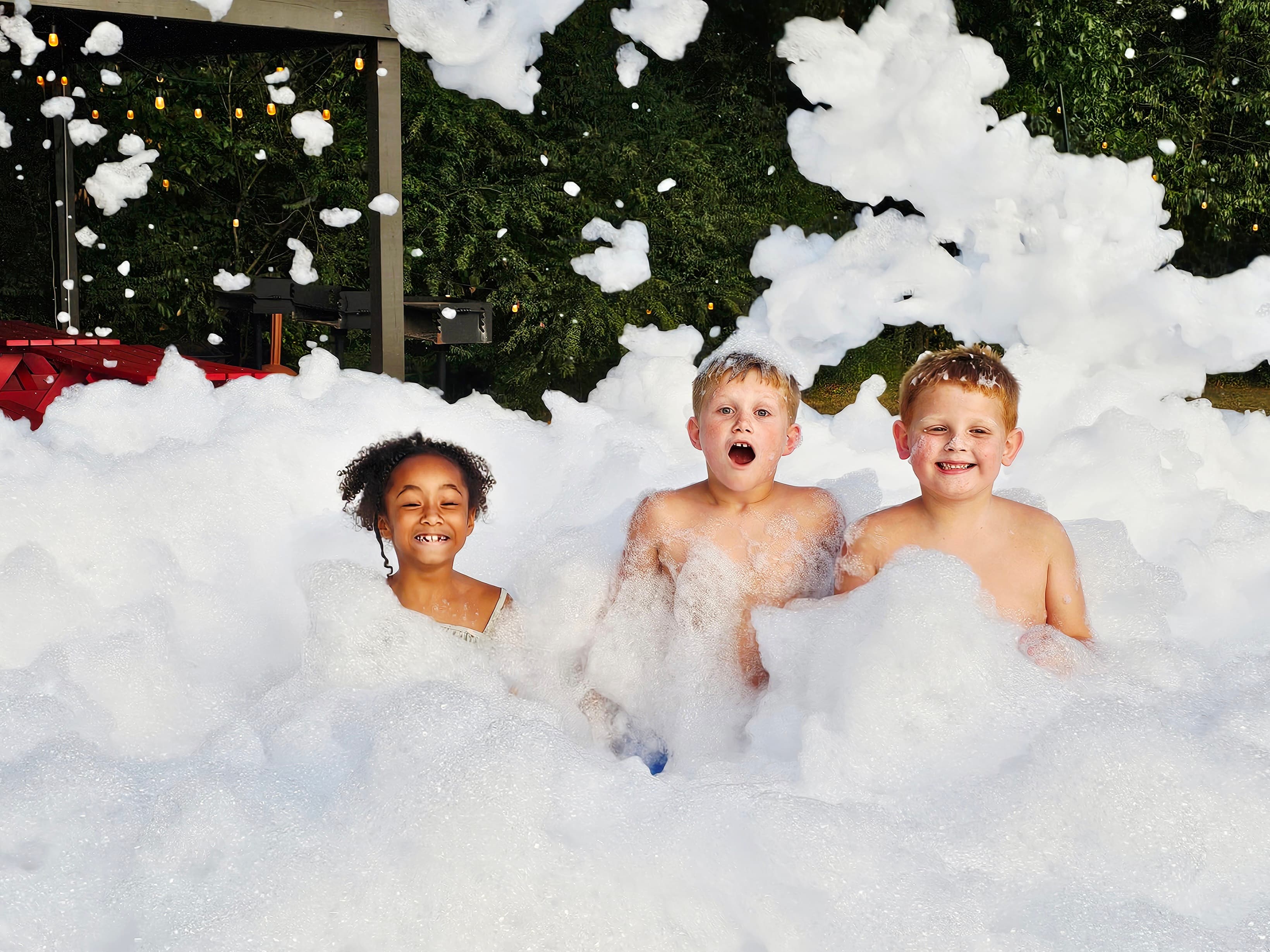 Three children play in a playful foam pit, smiling amid the bubbles.