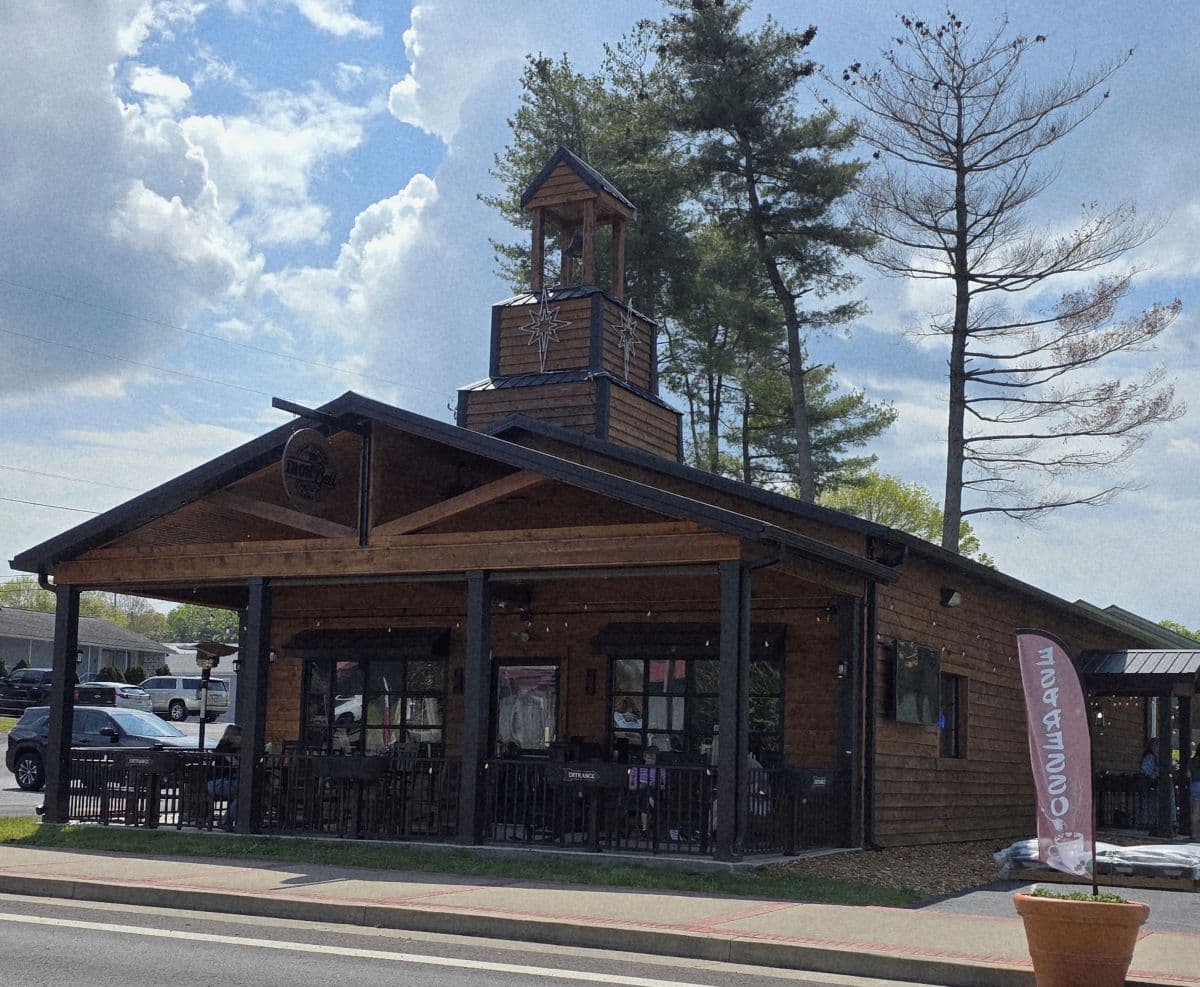 A rustic wooden restaurant with a tower and outdoor seating under a cloudy sky.