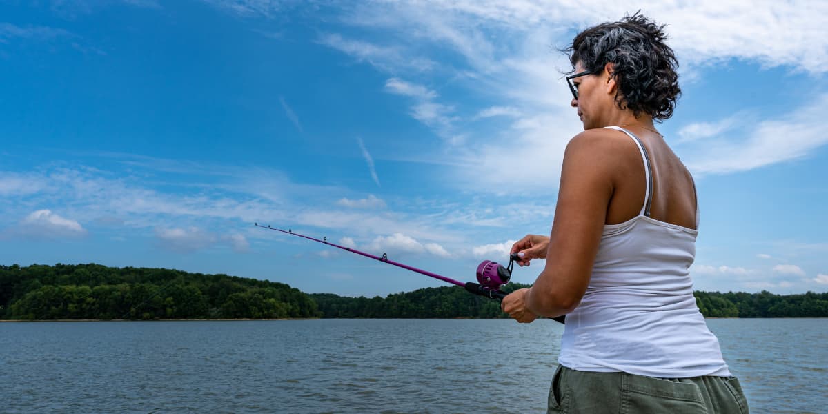 A person fishing by a serene lake under a blue sky.