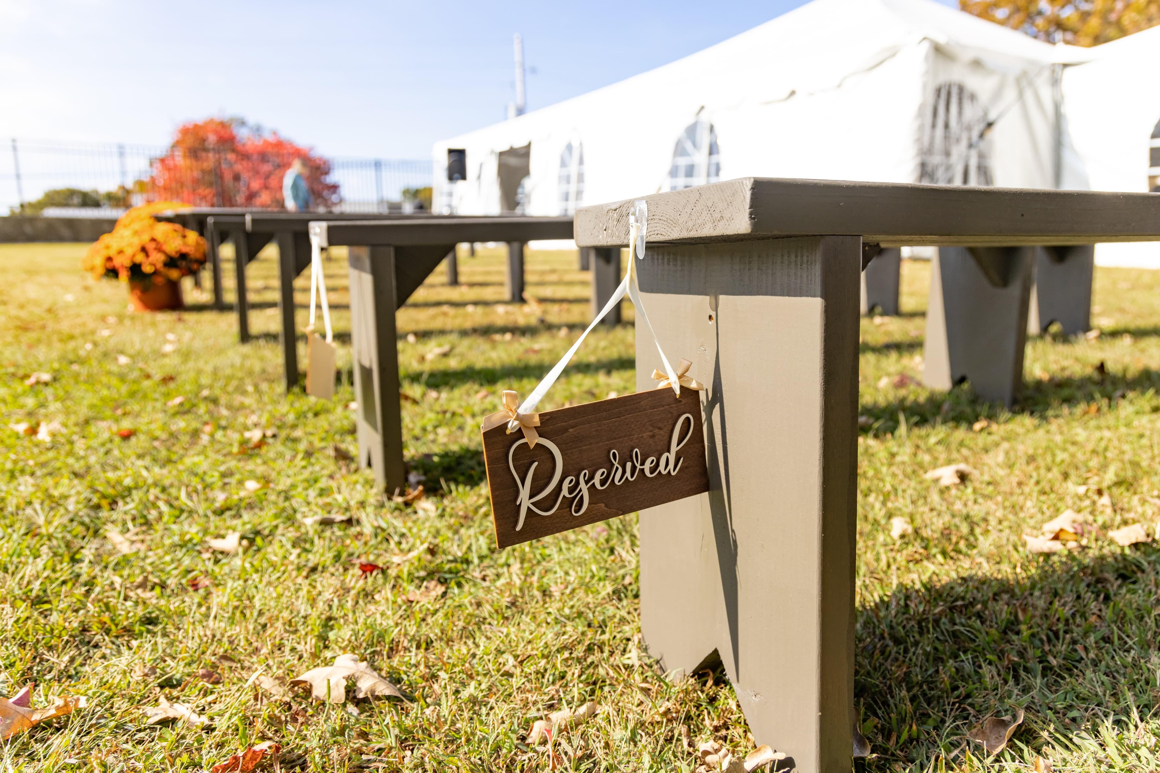 A wooden "Reserved" sign hangs from a picnic table in a grassy outdoor setting.