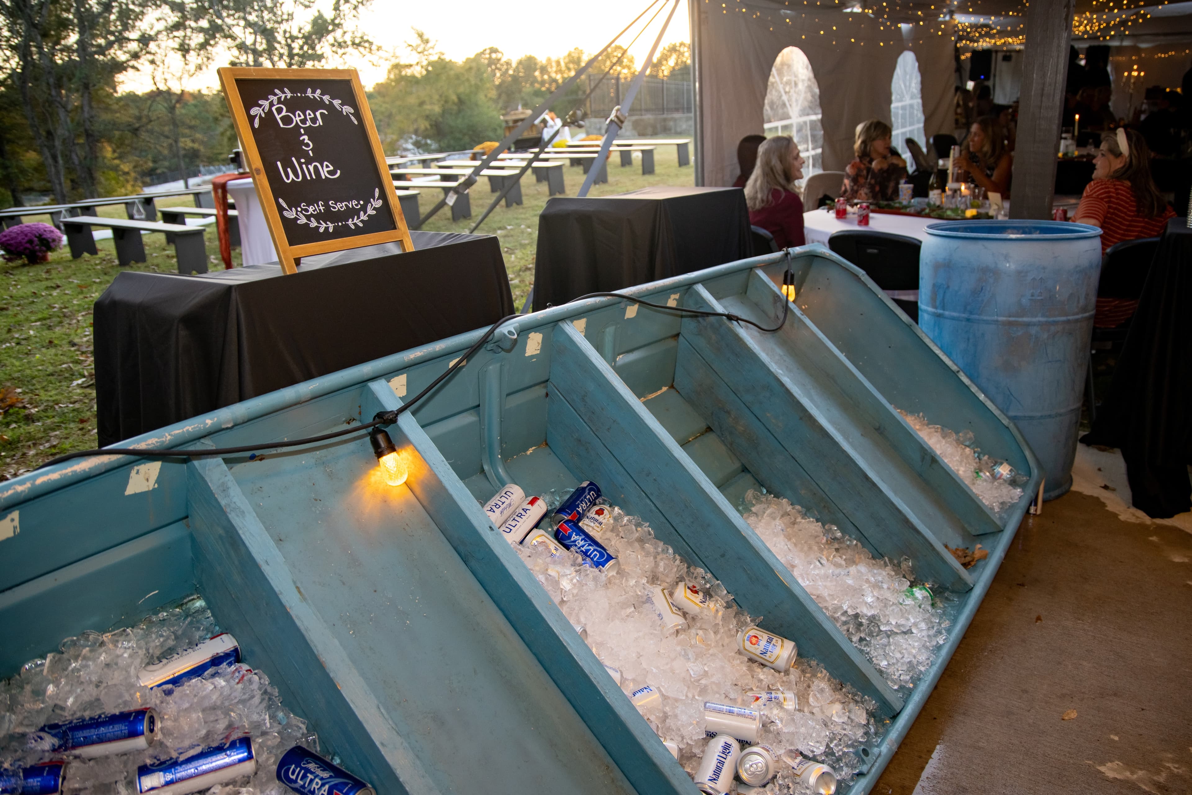 An old boat filled with ice and cans of beer, with a sign indicating a self-serve beer and wine station.