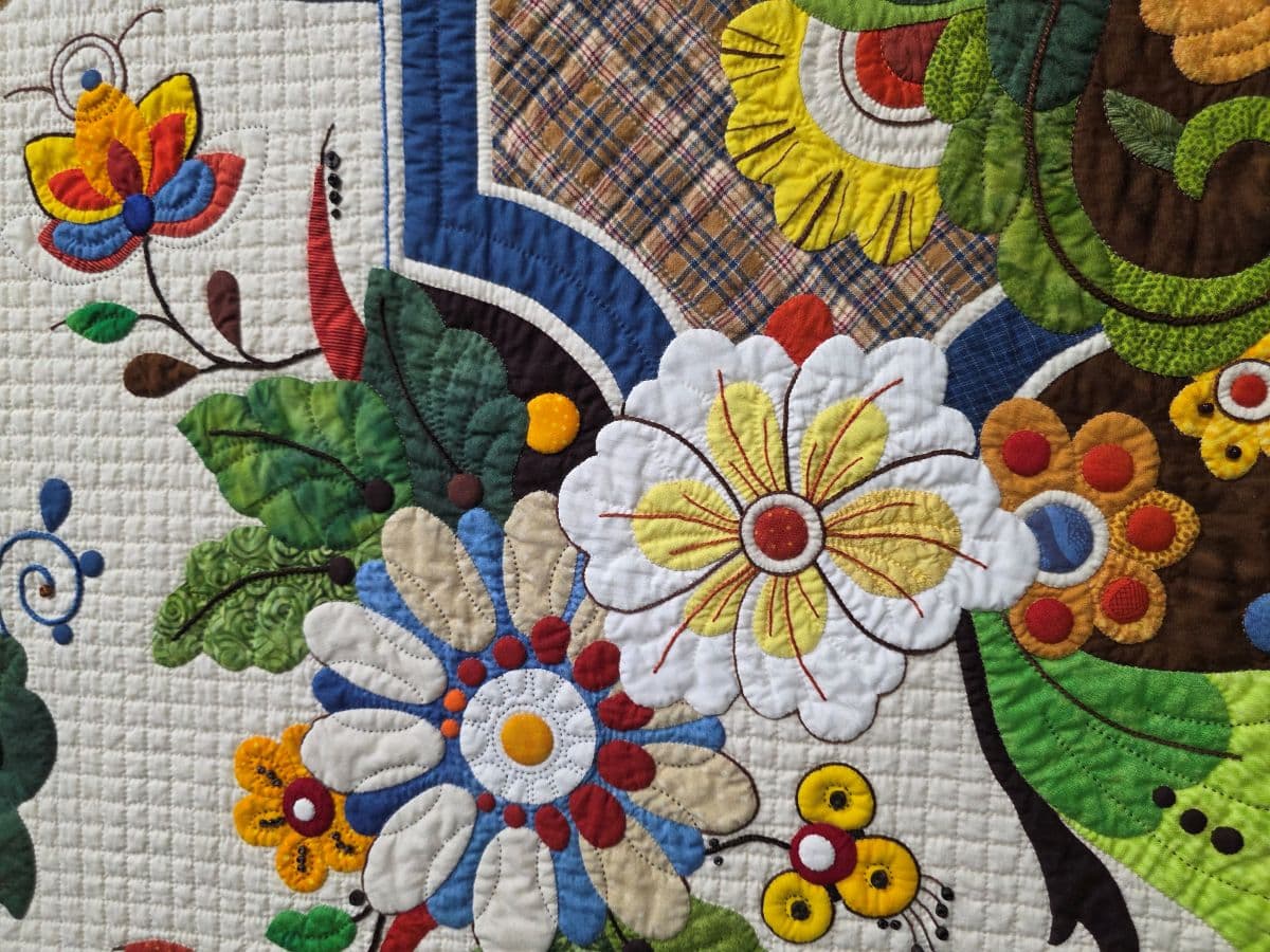 Brightly colored floral embroidery on a quilt featuring various flowers and leaves. Brightly colored floral embroidery on a quilt featuring various flowers and leaves.