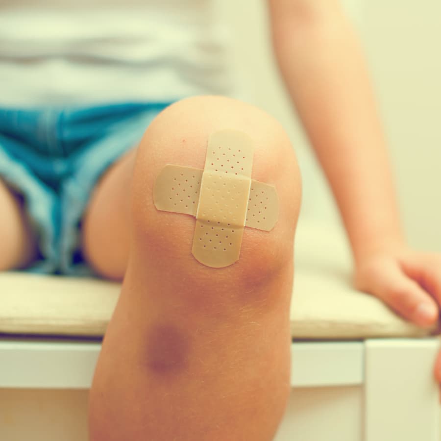 A child's knee is covered with a beige adhesive bandage.