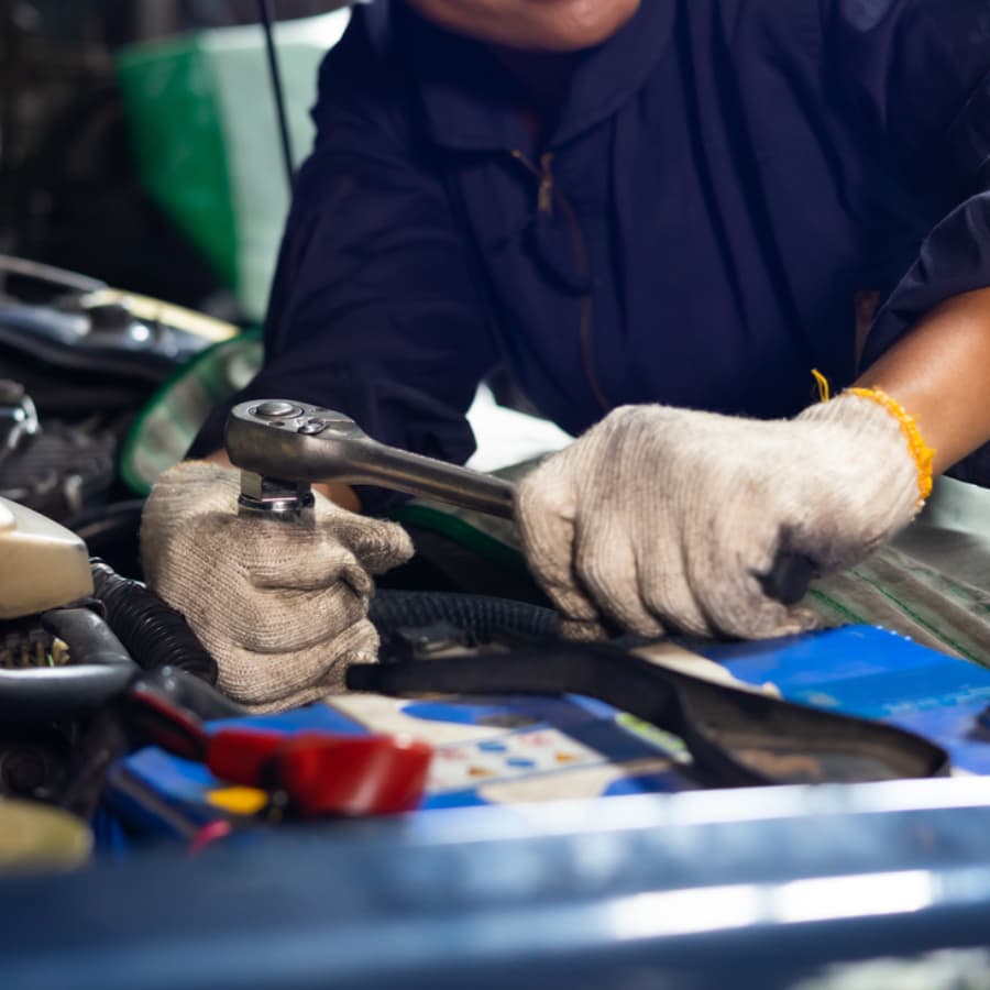A mechanic uses a ratchet tool on a vehicle's engine.