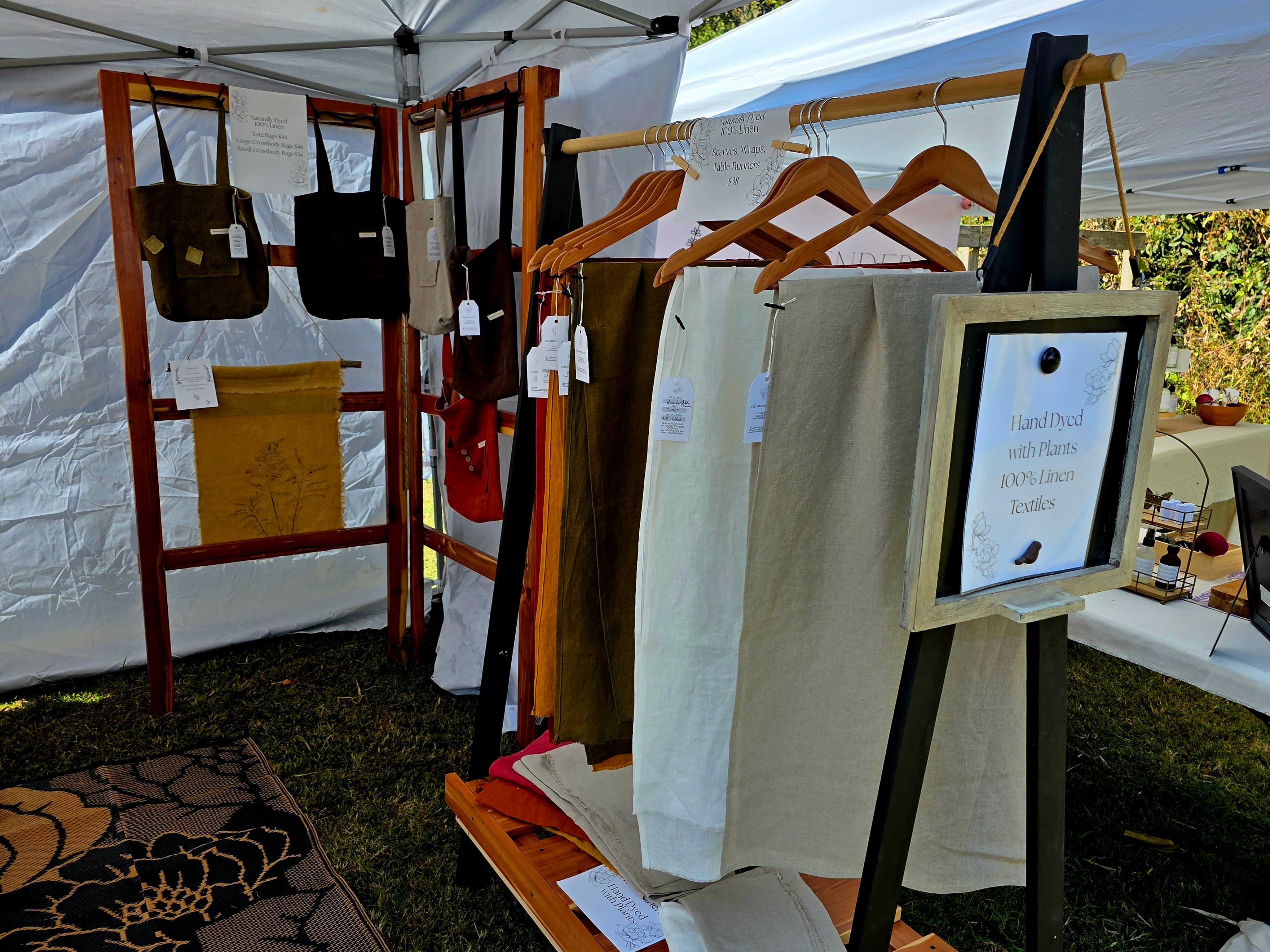 A display of handmade textiles and bags under a tent featuring various colors and styles.