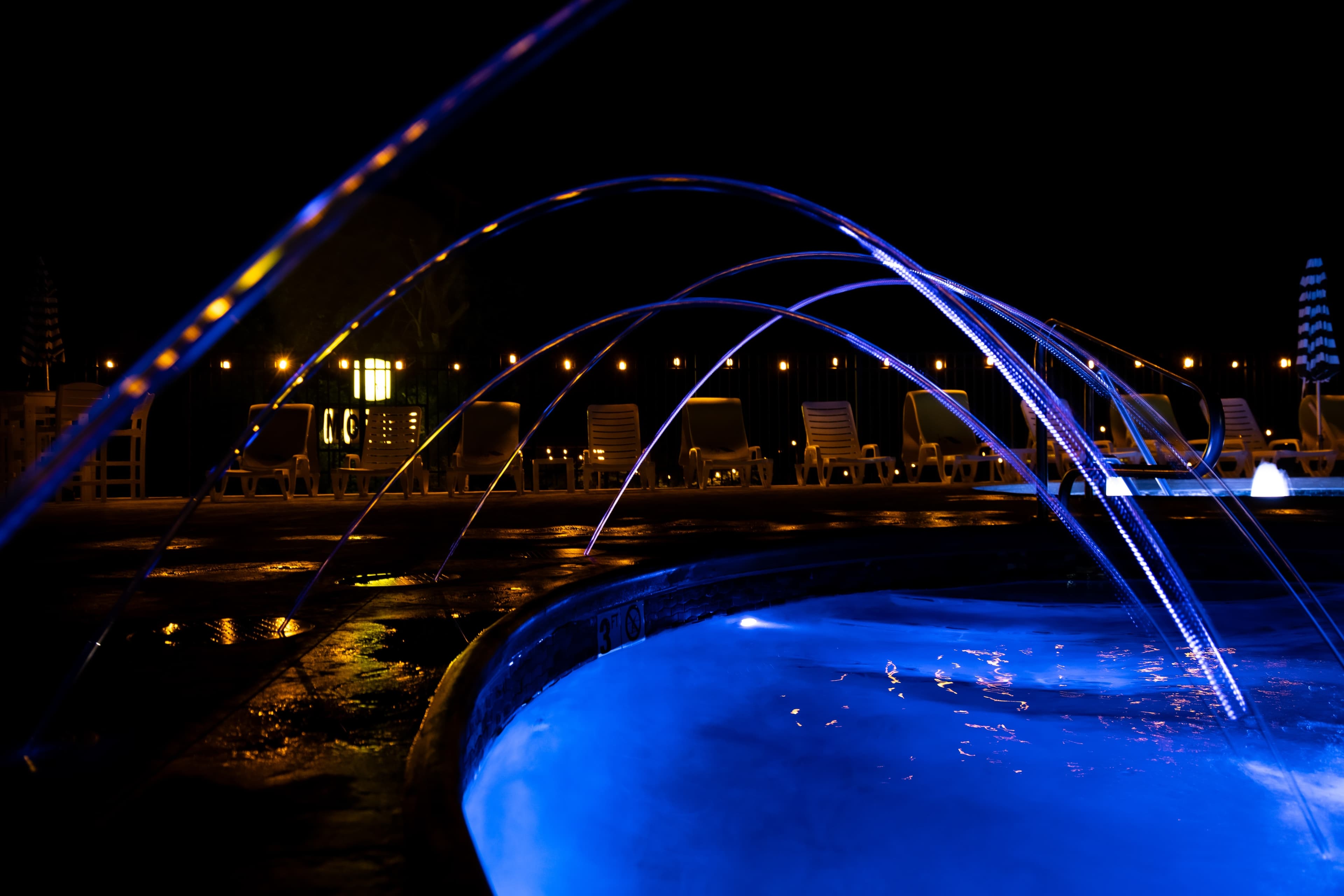 A lit pool with blue water and illuminated water jets at night.