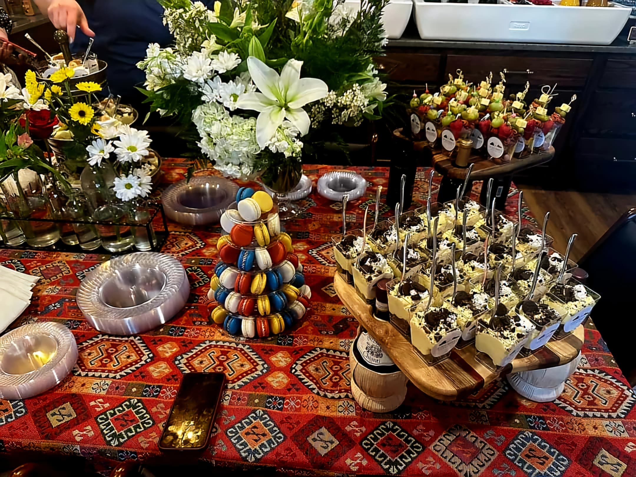 A colorful table spread featuring desserts, floral arrangements, and decorative dishes on a vibrant patterned tablecloth.