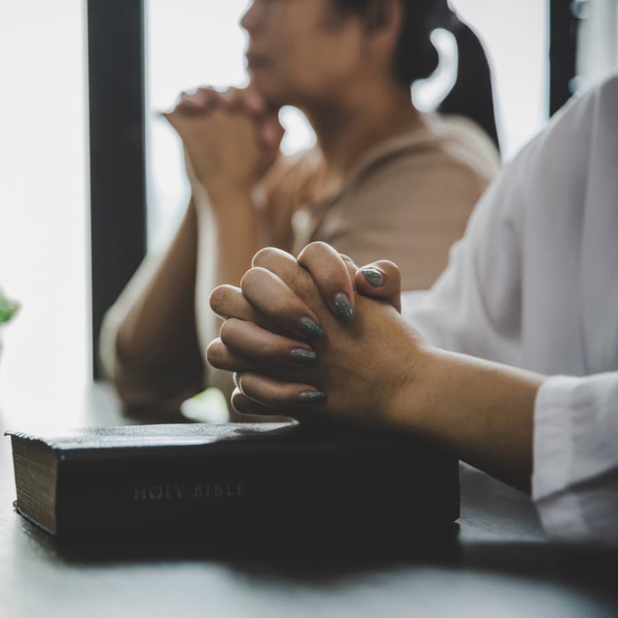 Two people praying with hands clasped over a Bible.