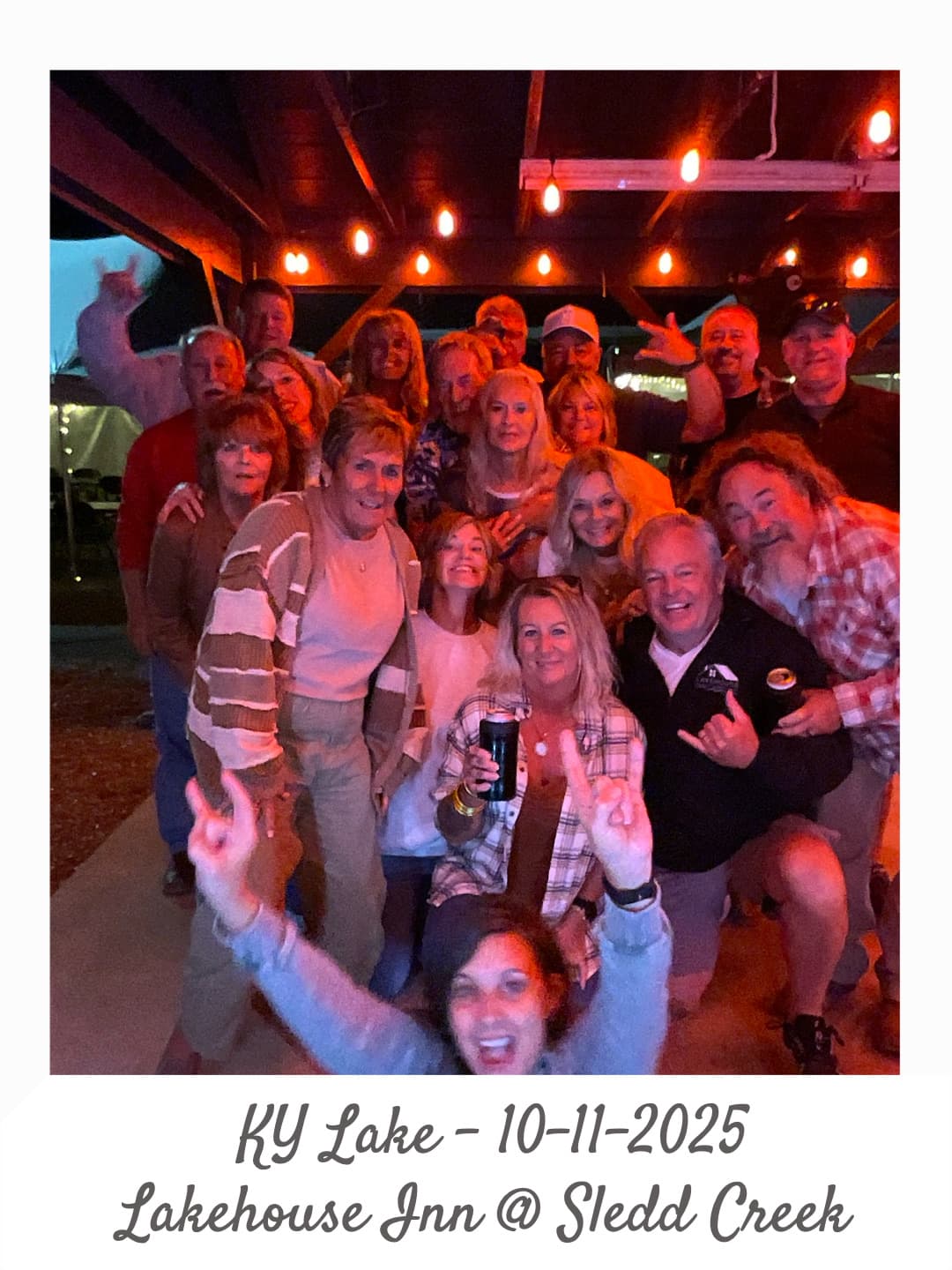 A large group of smiling friends gathers under string lights at Lakehouse Inn, KY Lake, on October 11, 2025.