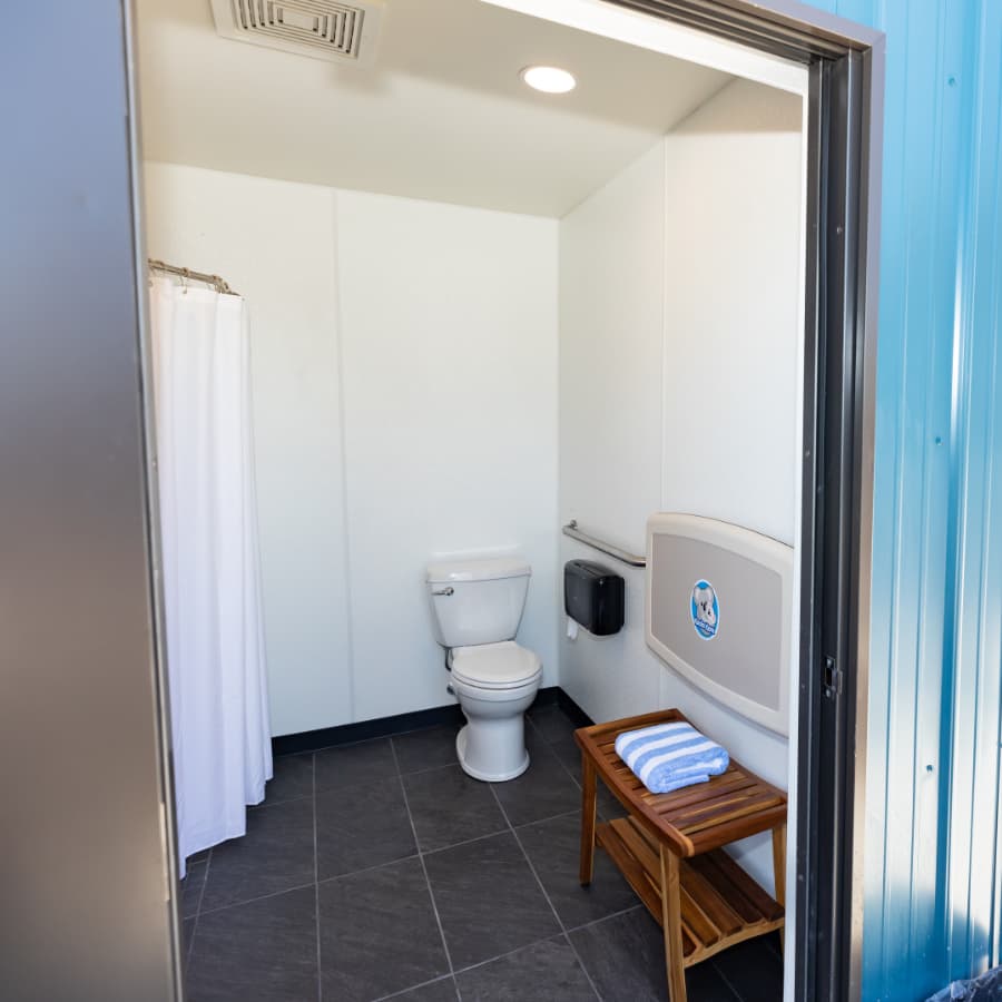 Interior view of a clean restroom featuring a toilet, a hand towel dispenser, and a wooden bench.