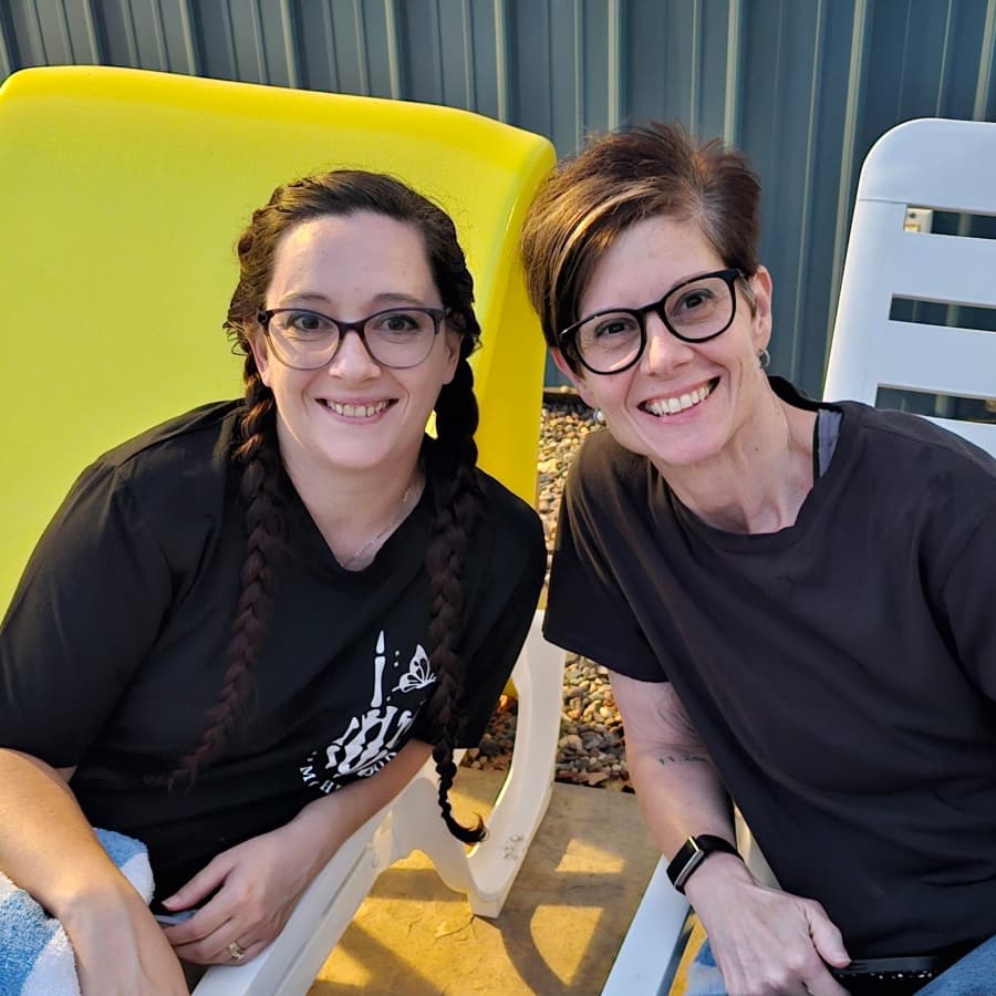 Two women smiling while sitting next to each other on lawn chairs.
