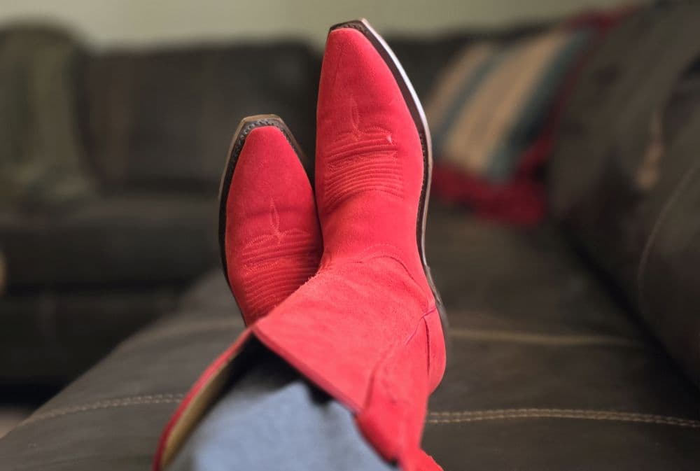 A pair of red cowboy boots resting on a couch.
