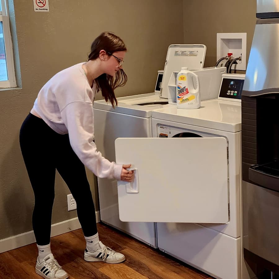 A person in a pink sweatshirt is loading a washing machine in a laundry room.