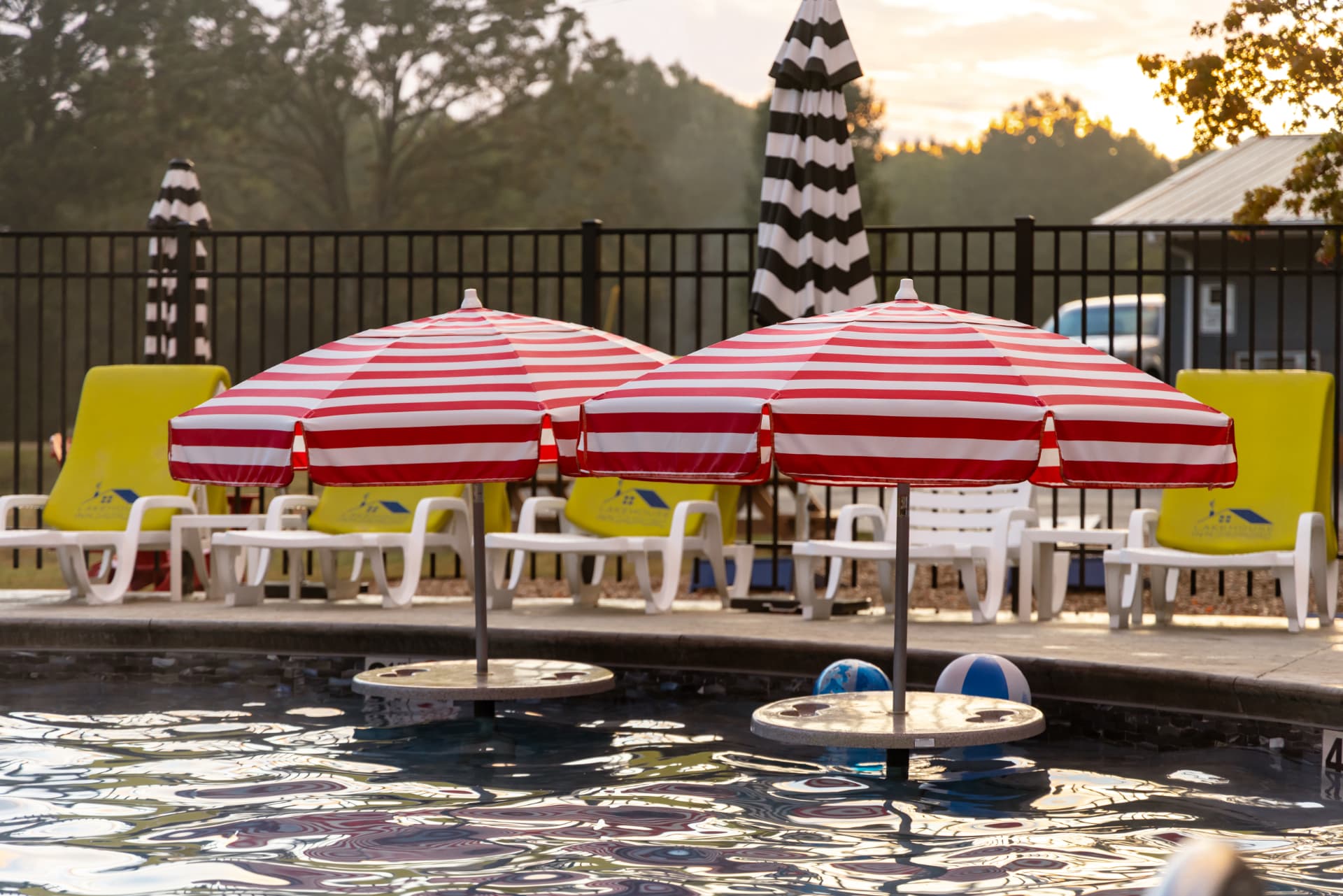 Two striped red and white umbrellas stand beside a pool, surrounded by lounge chairs and pool toys.