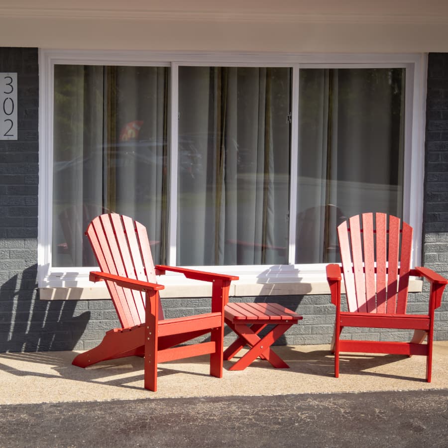 Two red Adirondack chairs and a small table are positioned in front of a window.