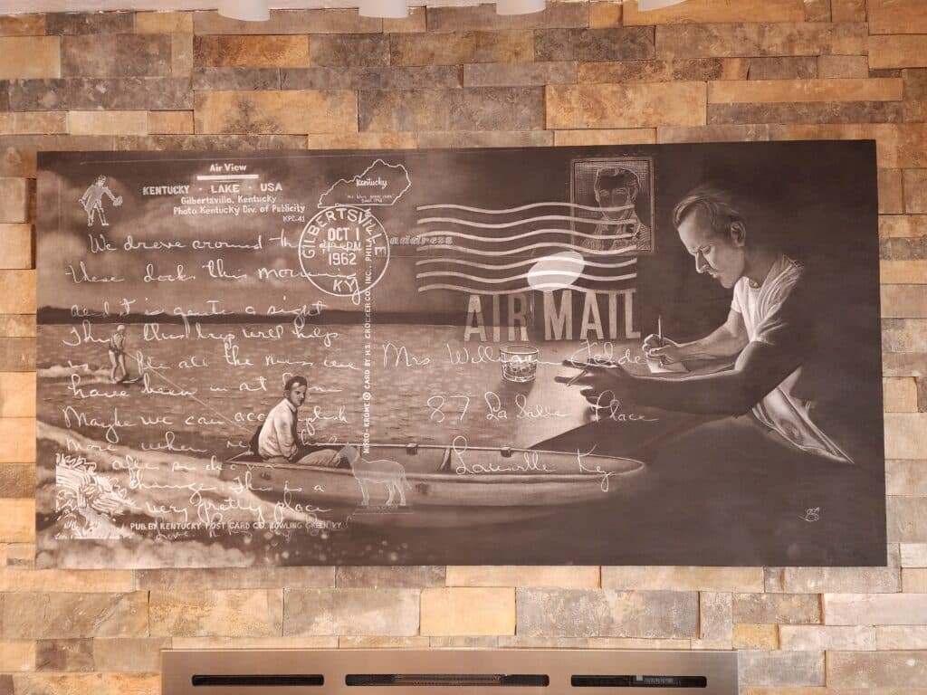 A black and white mural depicting a man writing a letter while another man is in a boat on a lake, surrounded by handwritten text and postal elements. A black and white mural depicting a man writing a letter while another man is in a boat on a lake, surrounded by handwritten text and postal elements.