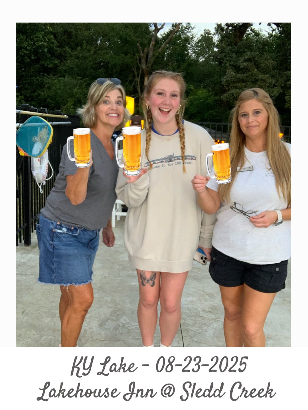 Three women smiling and holding drinks at a lakeside inn.