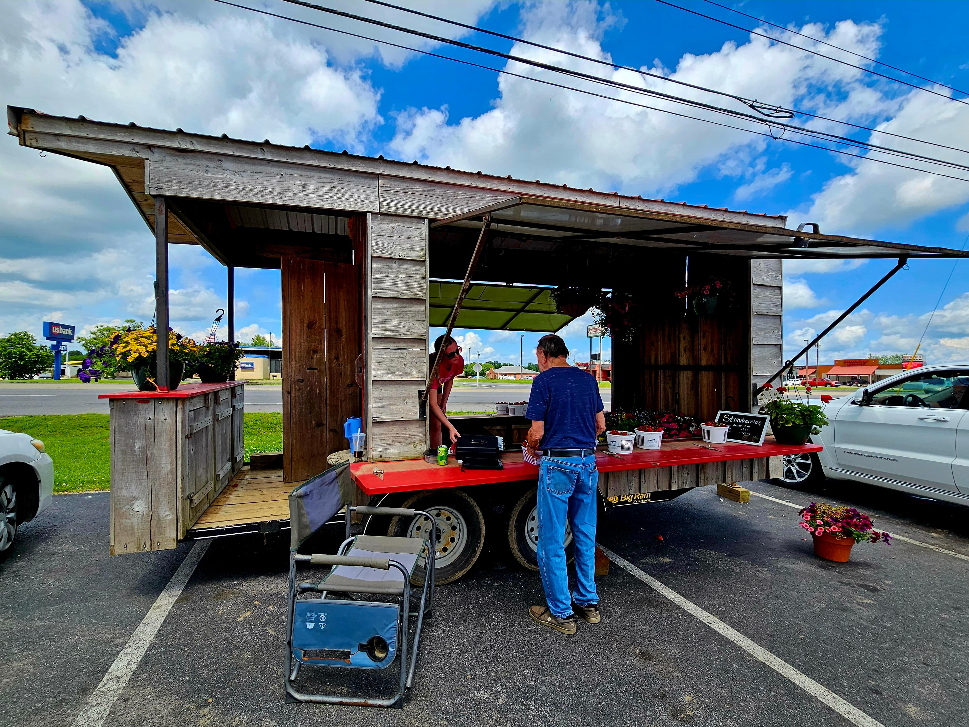 A rustic food truck with a wooden structure and a man preparing food outside under a blue sky.