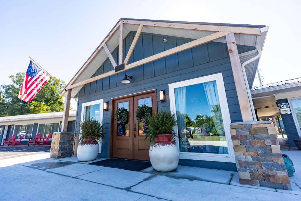 Exterior view of a charming blue building with a wooden awning, potted plants, and an American flag.