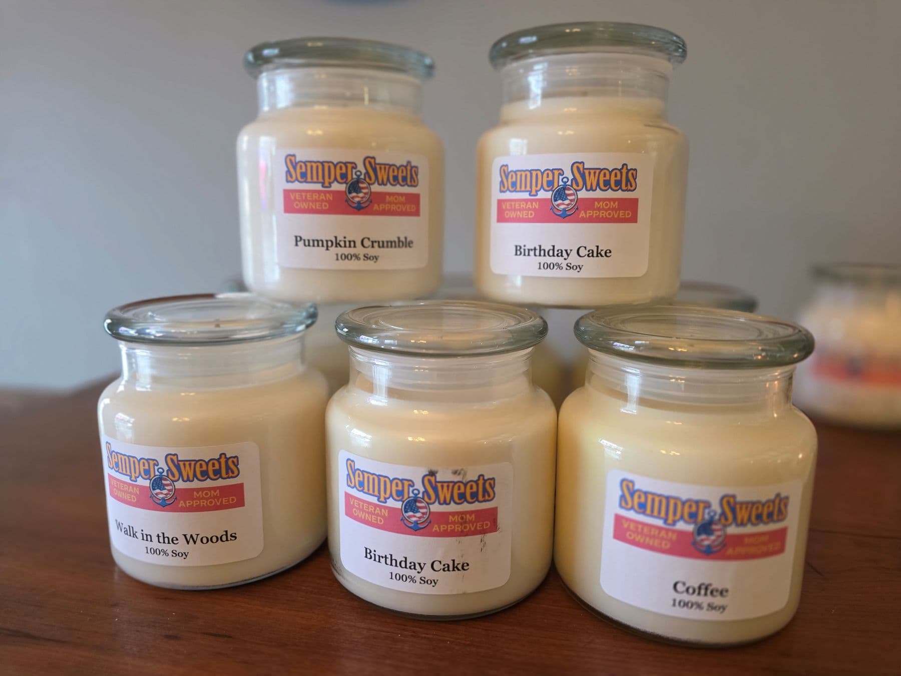 A display of six scented soy candles with labels for "Pumpkin Crumble," "Birthday Cake," "Walk in the Woods," and "Coffee."