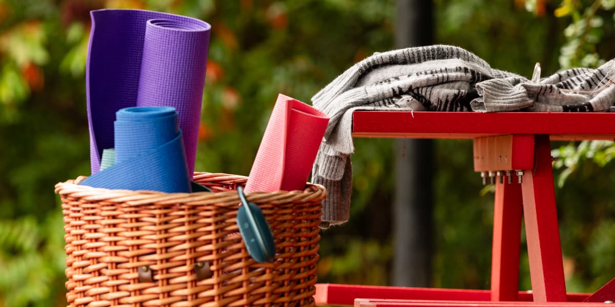 A basket of colorful yoga mats beside a red table with a folded blanket.