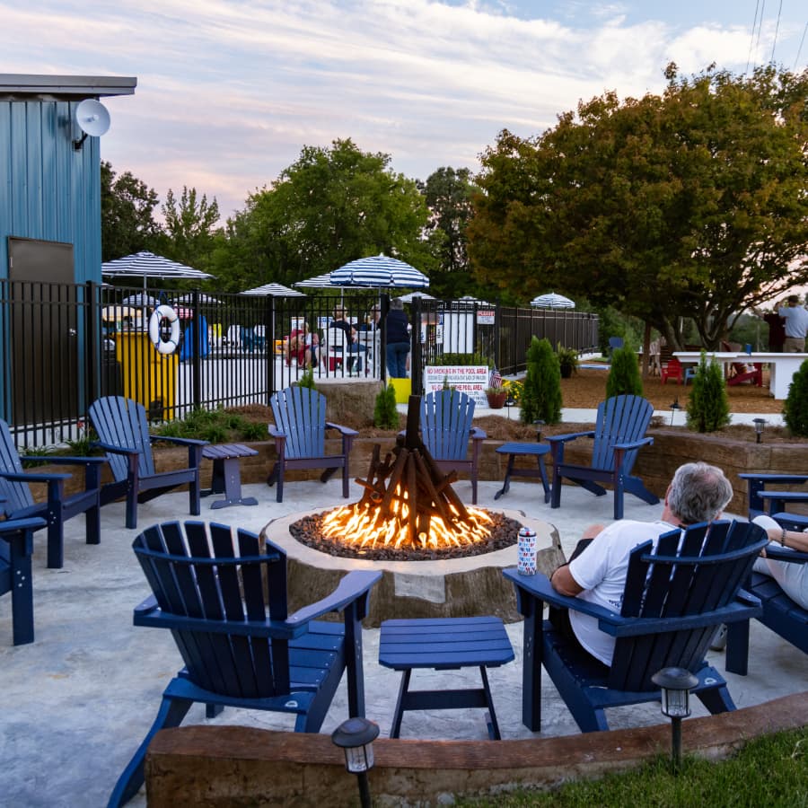A cozy outdoor seating area surrounds a fire pit, with people enjoying the ambiance in the background.