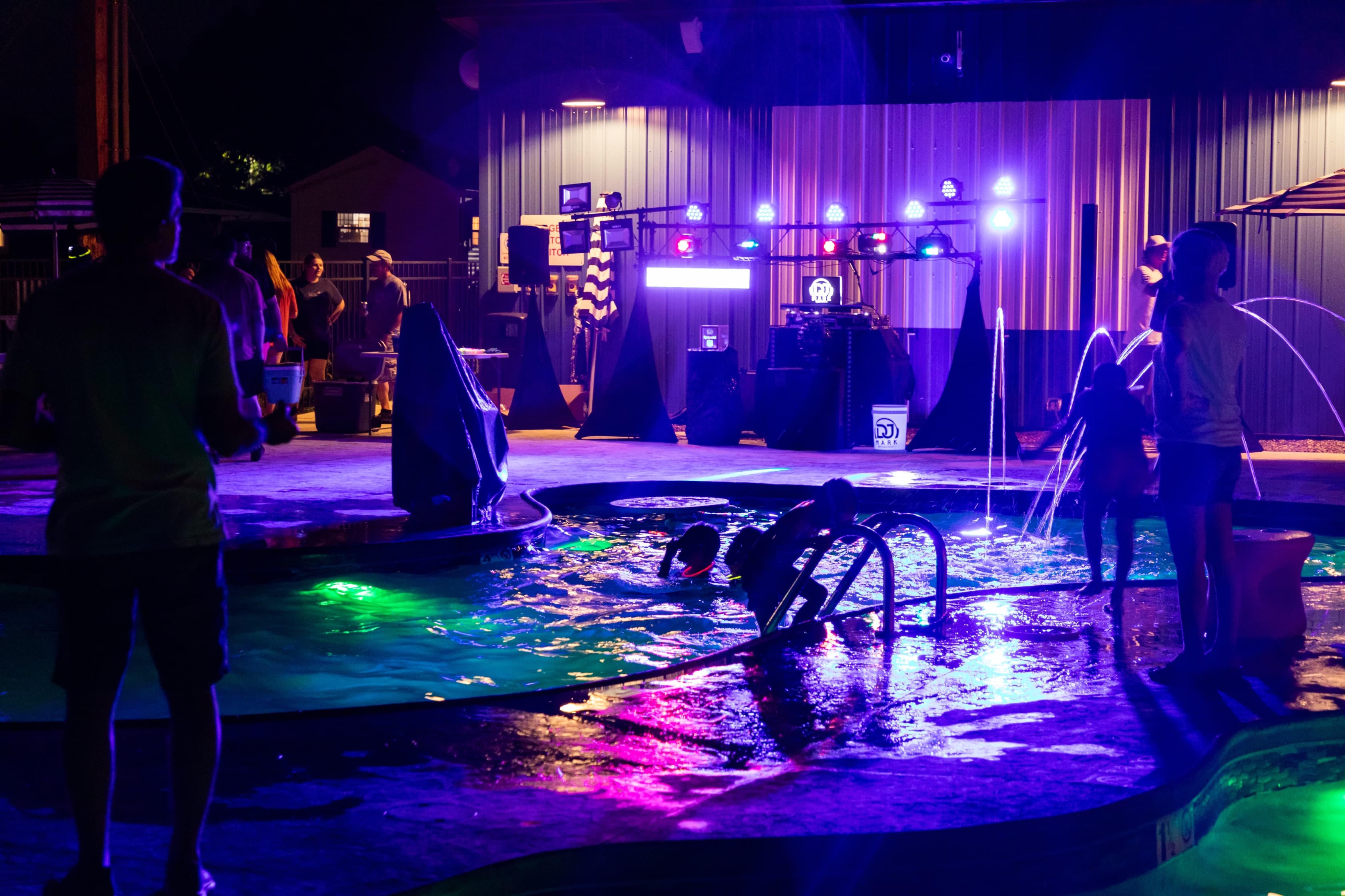 A vibrant nighttime scene at a pool party with colorful lights and people enjoying the atmosphere.