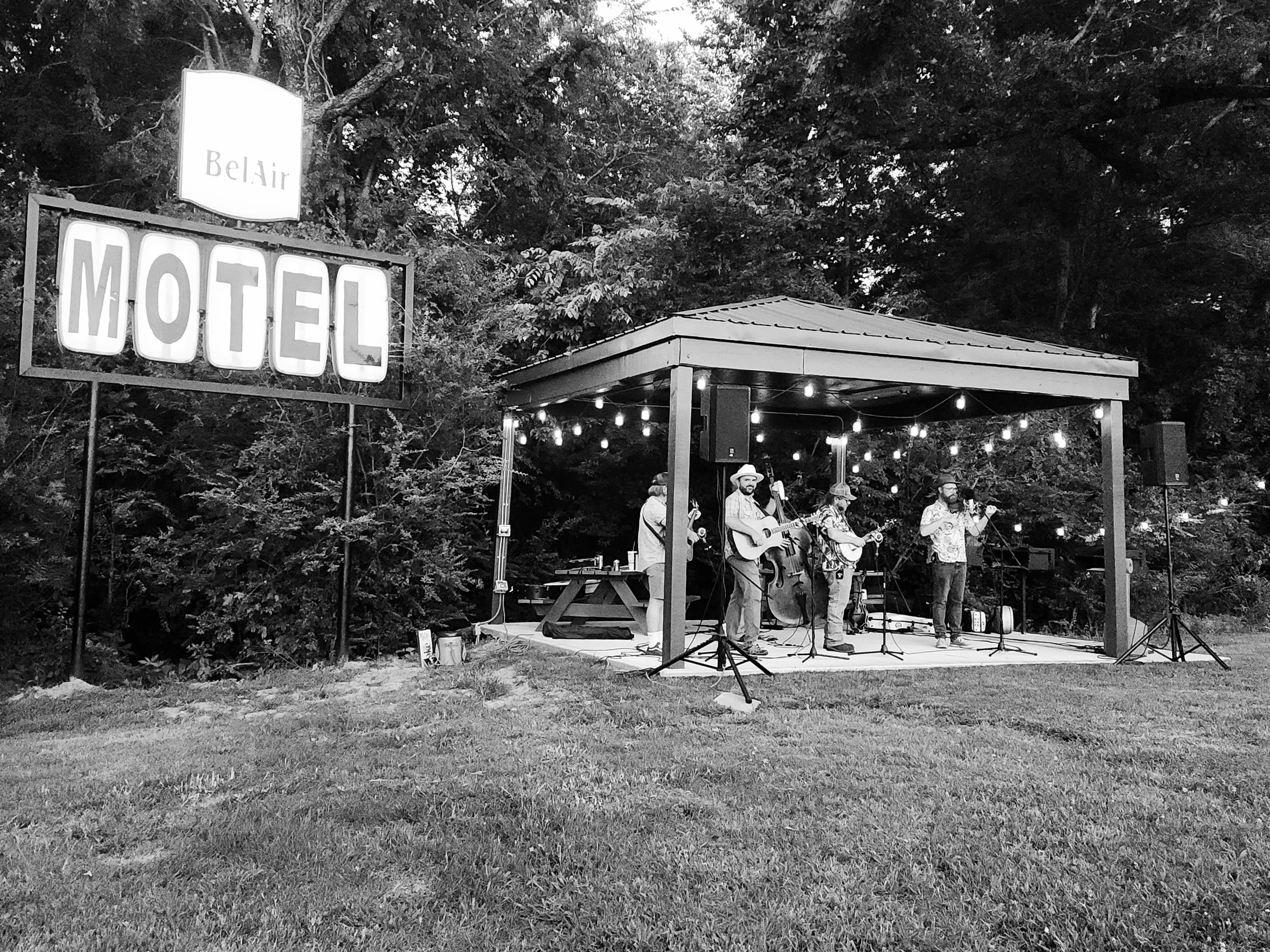 A black-and-white photo of a live band performing under a pavilion near a "Bel Air Motel" sign.