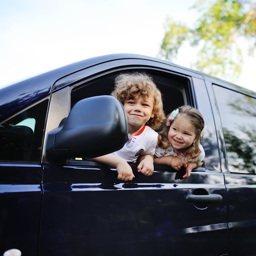 Two cheerful children peek out of a car window.