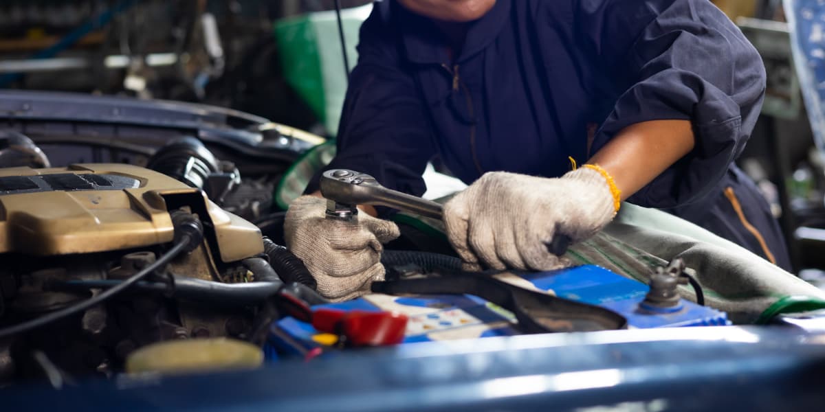 A person in gloves is using a wrench to work on a car engine.