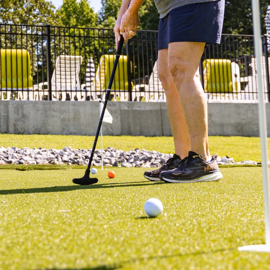 A person is putting on a mini-golf course with colorful balls nearby.
