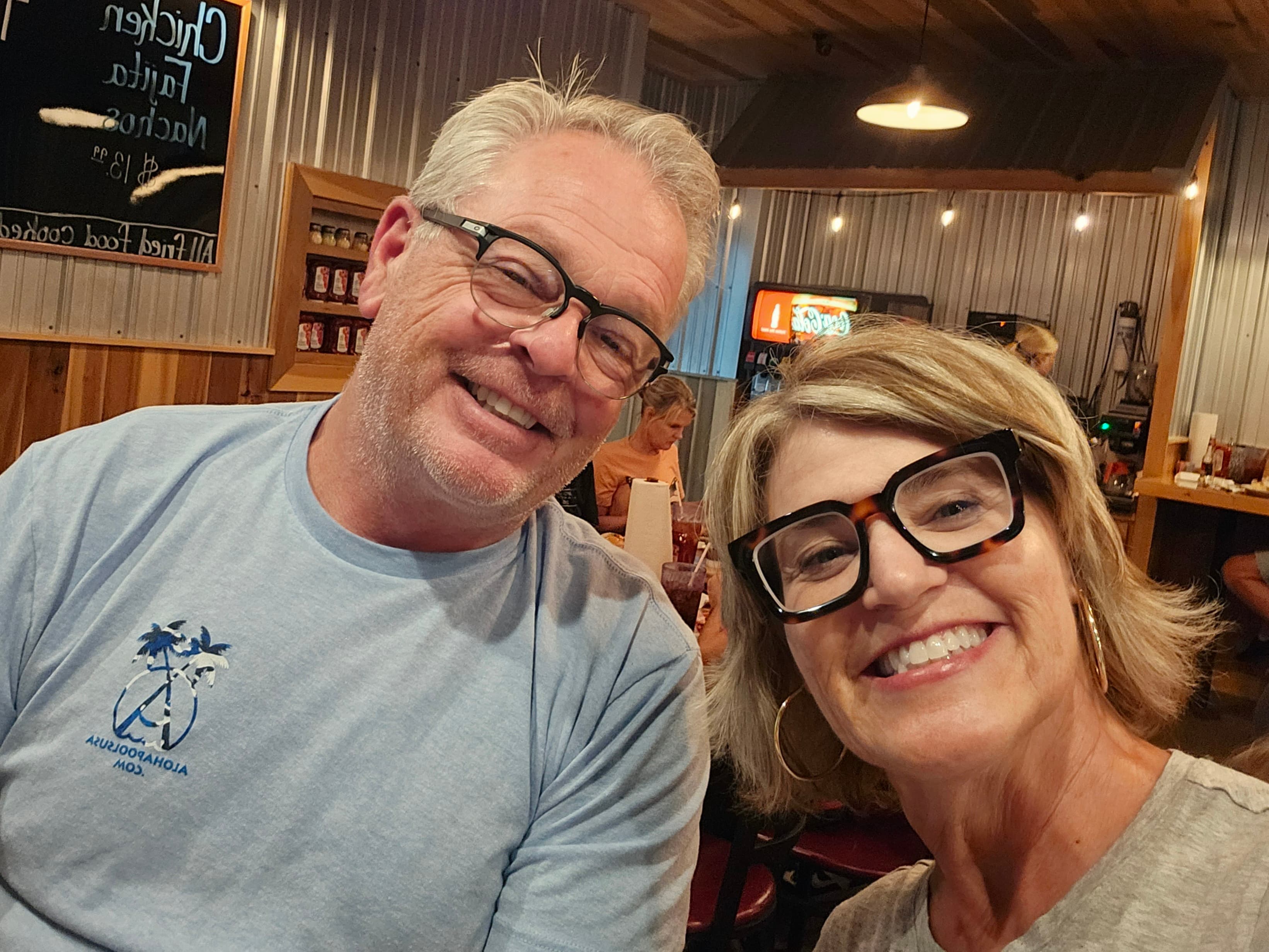A man and a woman smile at the camera while sitting in a casual restaurant.