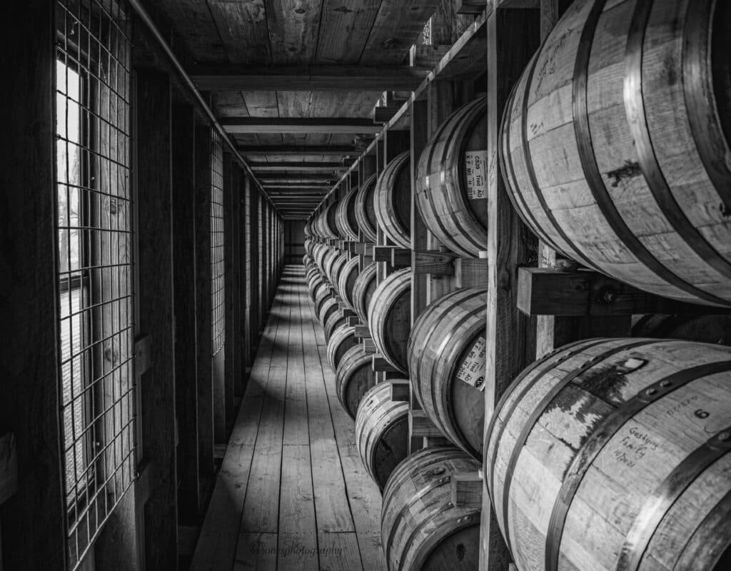 A series of wooden barrels lined up along a narrow corridor in black and white.