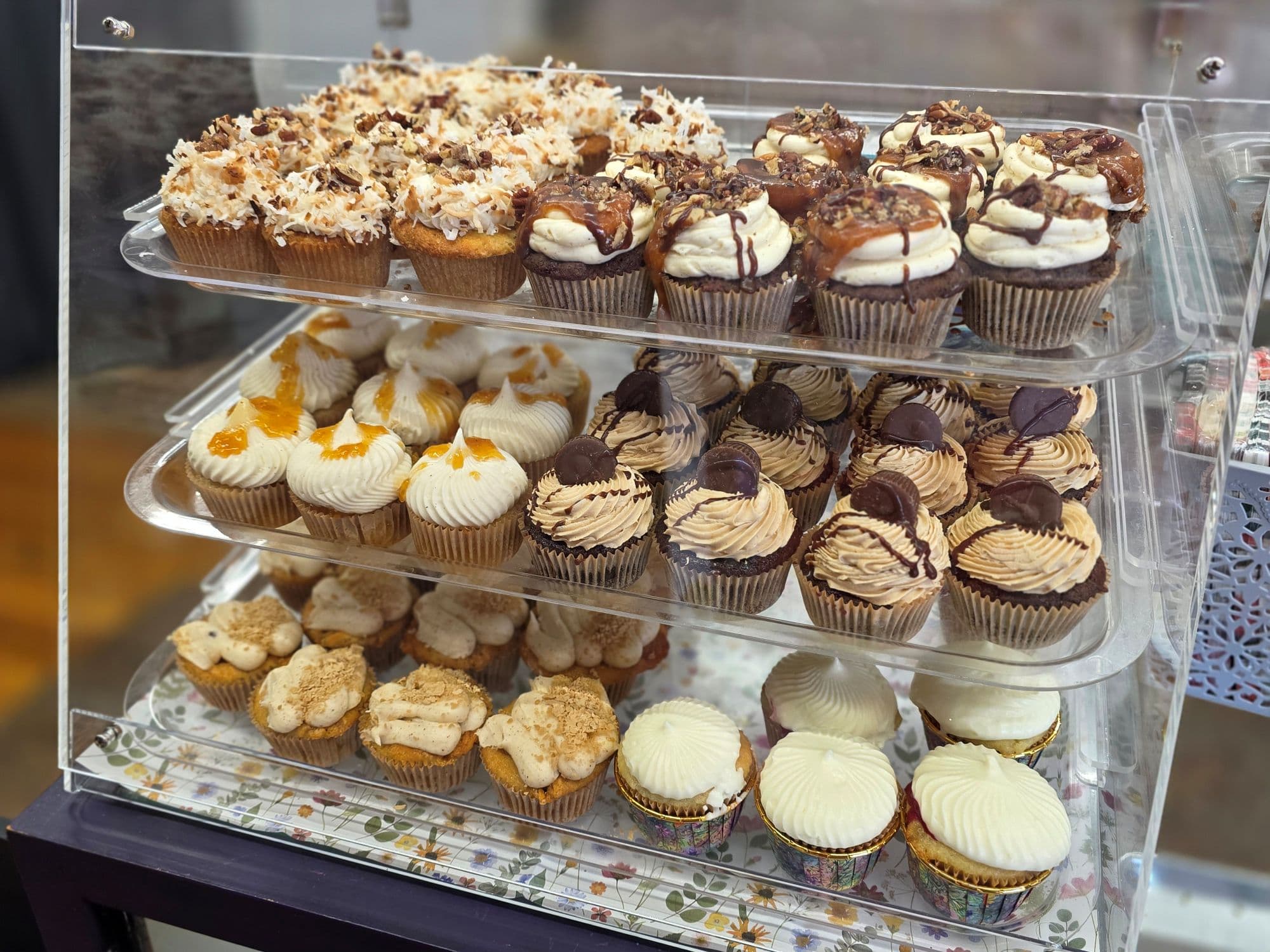 A display case filled with assorted cupcakes, featuring various toppings and flavors.