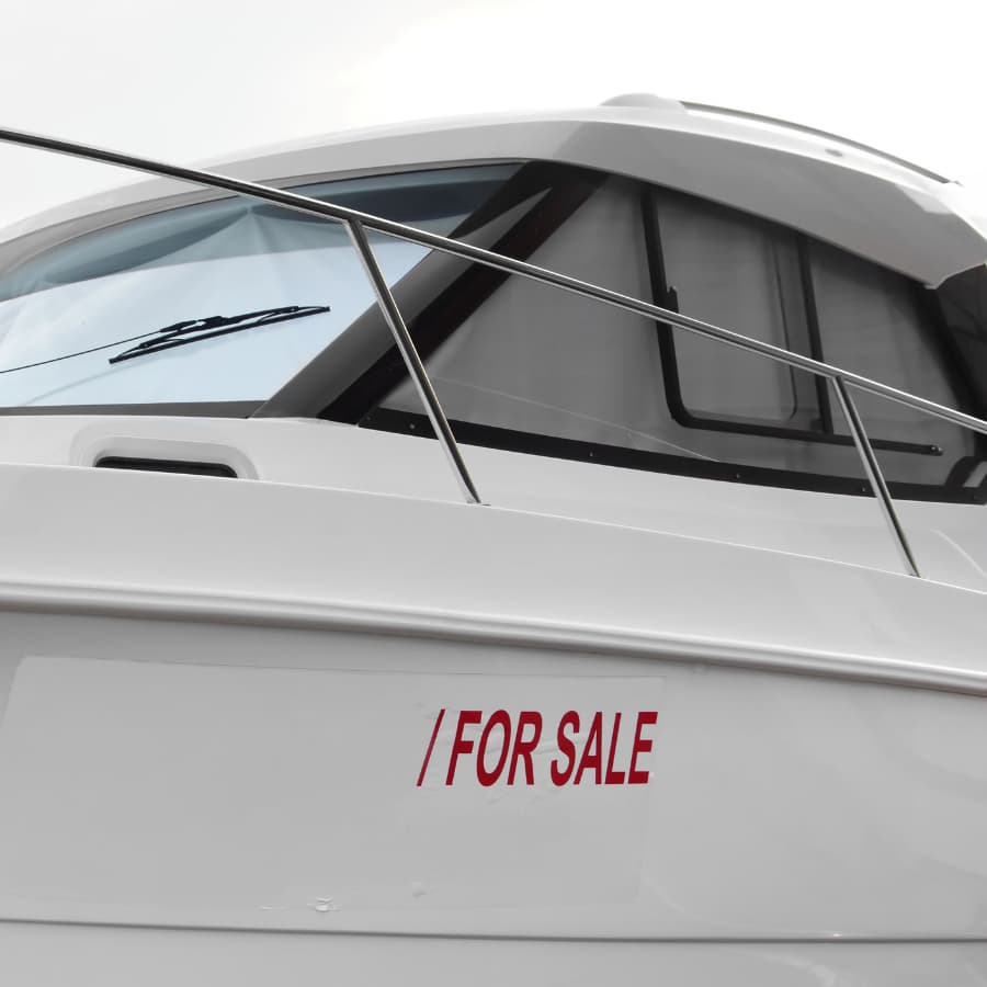 A white boat with a red "FOR SALE" sign on its side.