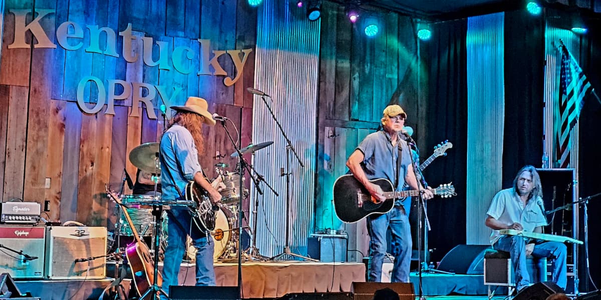 A country band performs on stage at the Kentucky Opry with musical instruments and colorful lighting.
