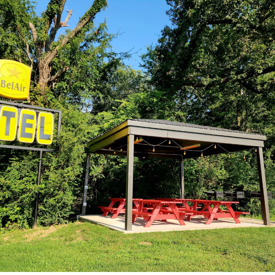 A red picnic area with a gazebo and a motel sign in a lush green setting.