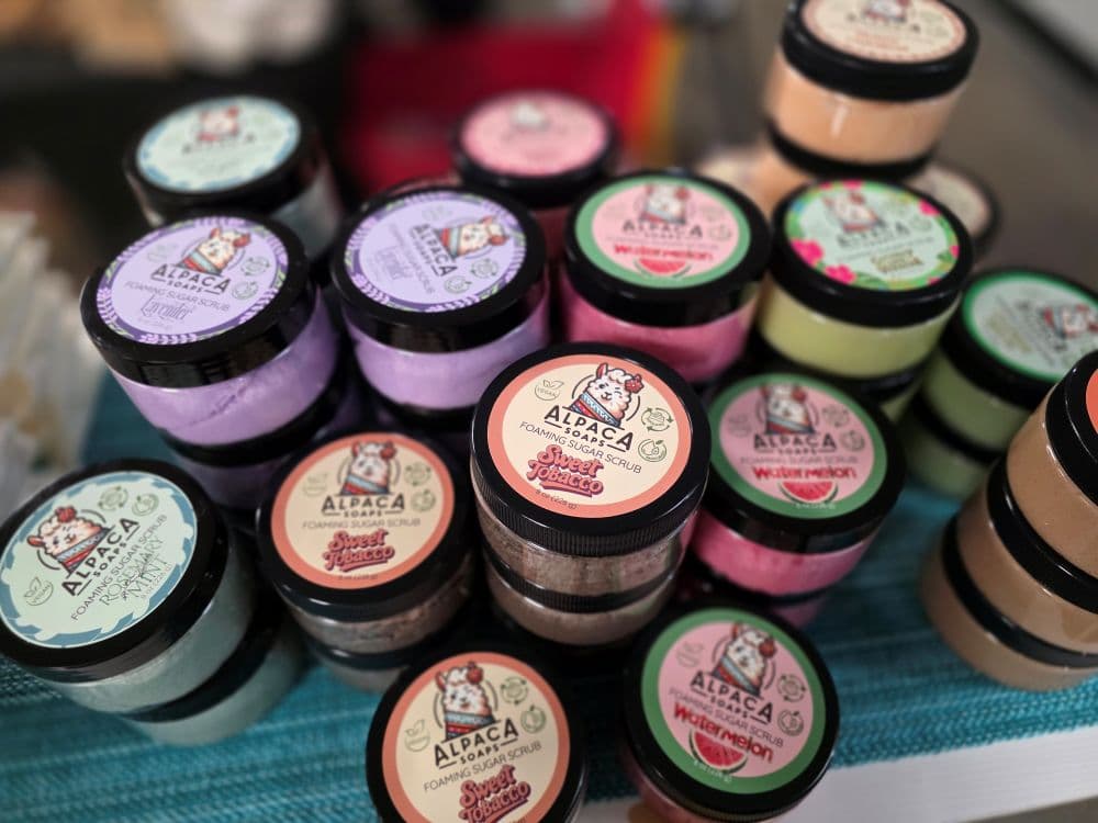 A variety of colorful jars of Alpaca body scrubs are stacked on a table.