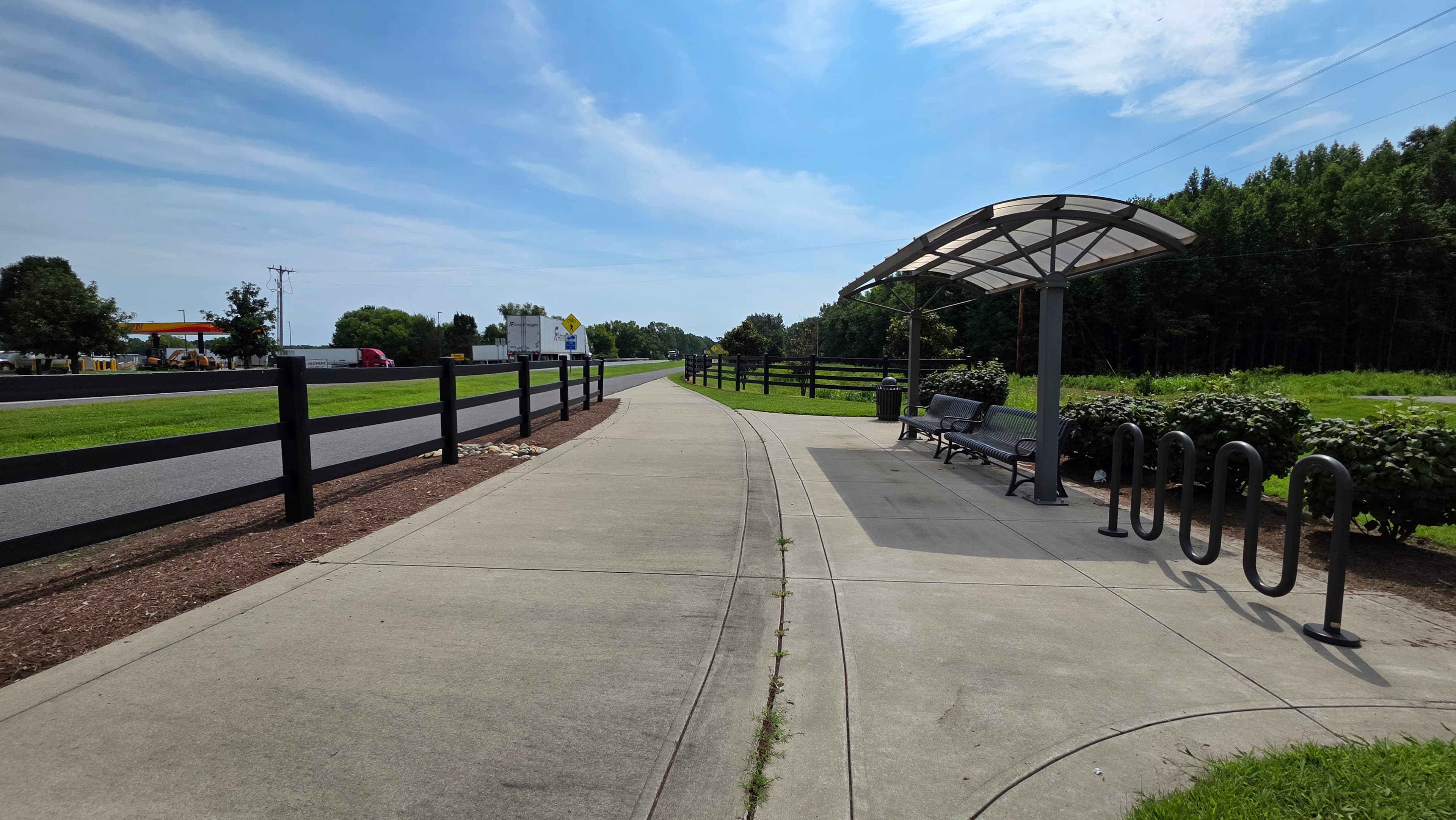 A paved path lined with greenery and bike racks, featuring a bus stop shelter under a clear sky.