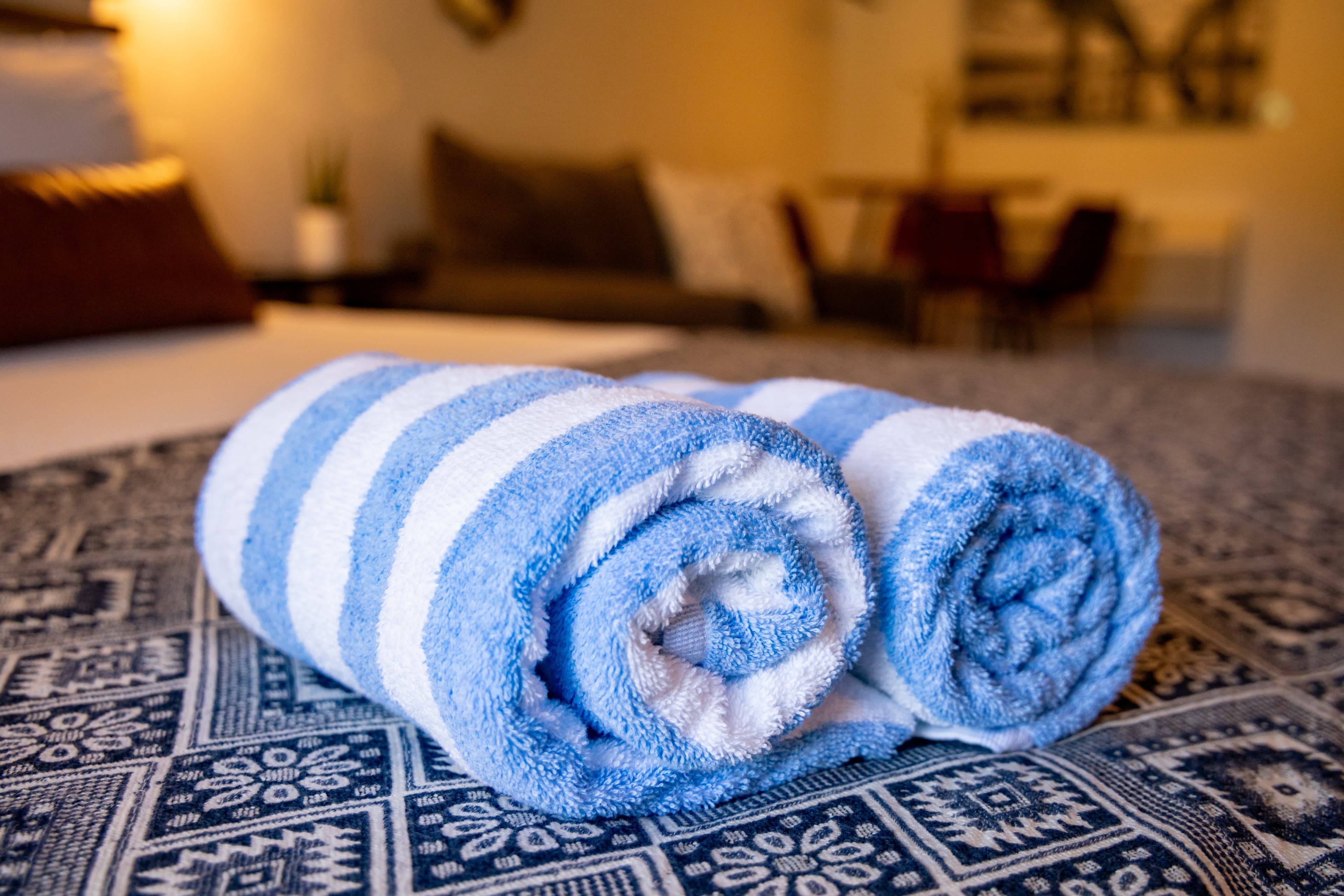 Two neatly rolled blue-striped towels on a patterned tablecloth.
