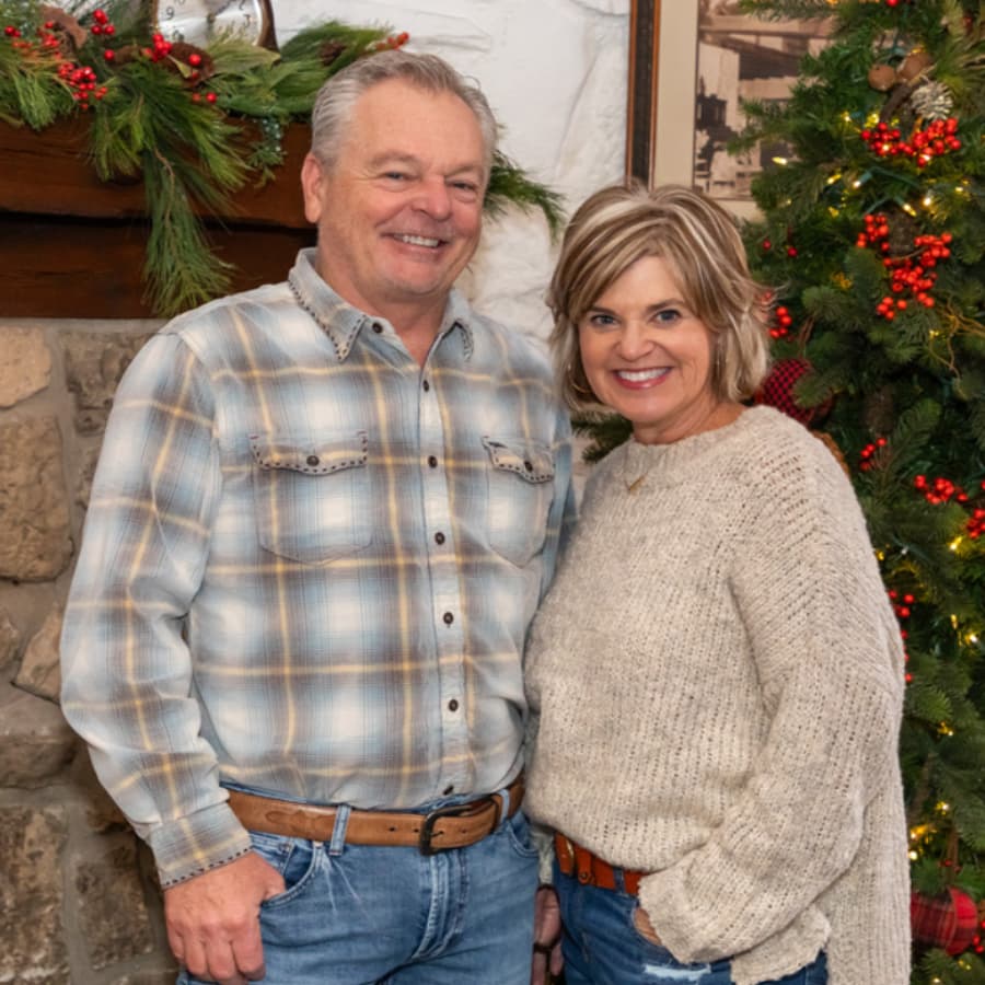 A smiling couple poses together in front of a festive, decorated backdrop.
