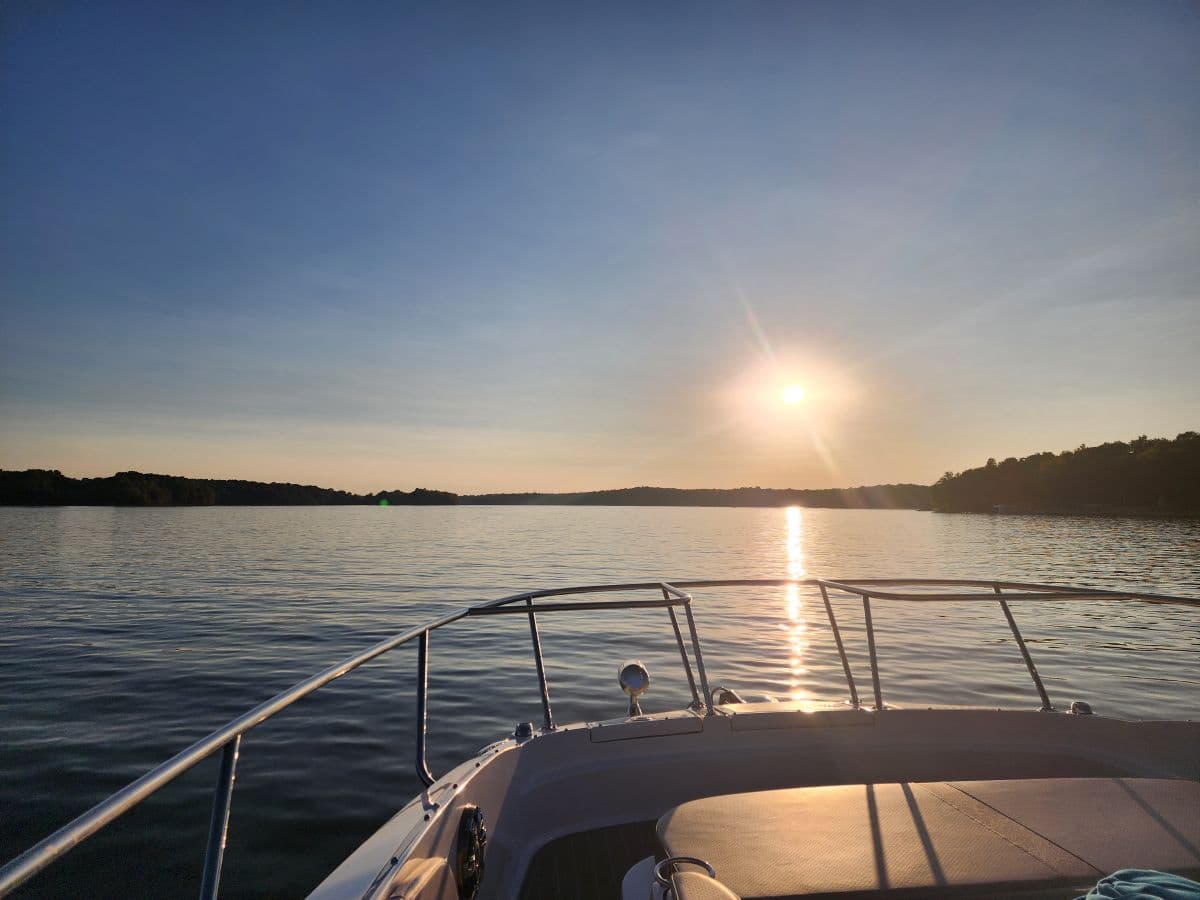 view of a sun setting over a lake from the front of a cabin cruiser boat