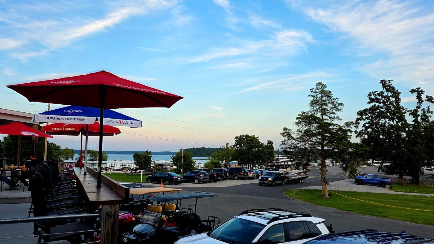 view of a lake with blue skies from a patio dotted with red and blue umbrellas