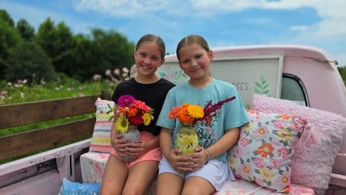 two girls sitting in the back of a truck holding colorful bouquets of flowers